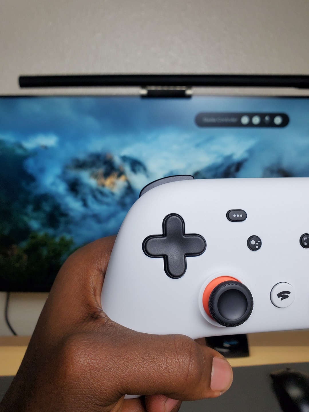 Stadia gaming controller held by a left hand in front of the screen