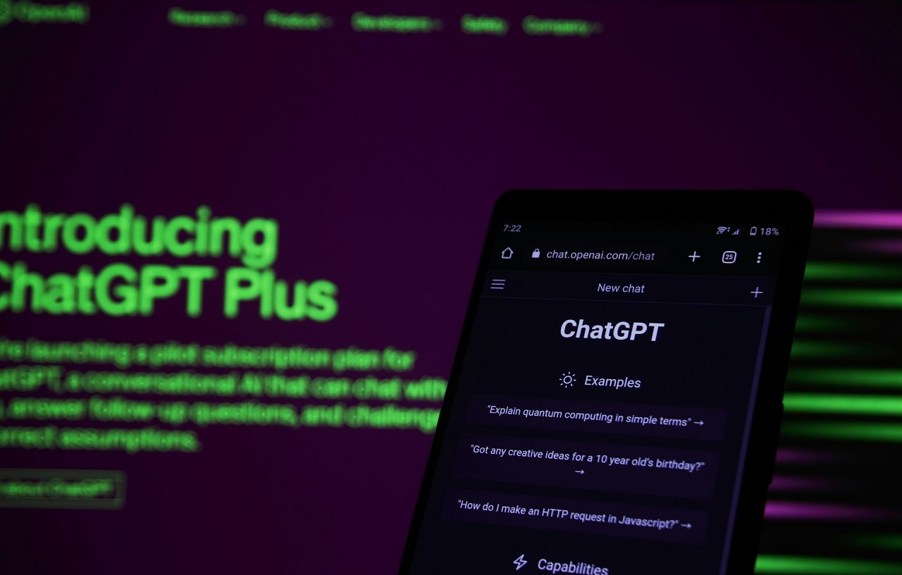 ChaptGPT on a smartphone and a blurred screen on the background with the words ‘Introducing ChatGPT Plus’